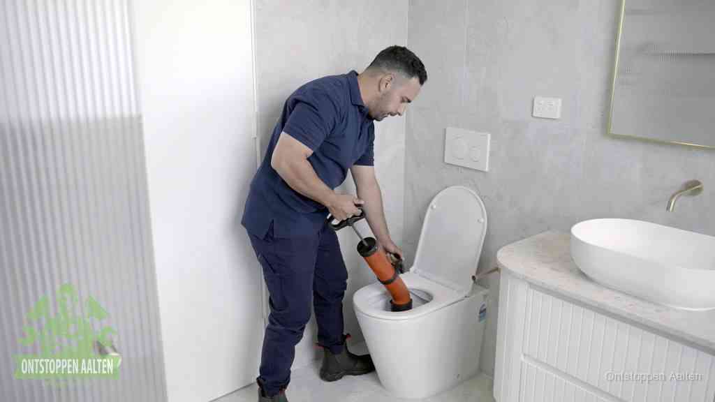 Een monteur buigt over een wandcloset en duwt met de hand een persluchtontstopper in de toiletpot om de verstopping handmatig los te maken in Aalten