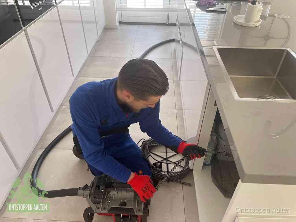 Een monteur ontstopt de keukenafvoer onder de spoelbak met een elektrische veermachine in Aalten