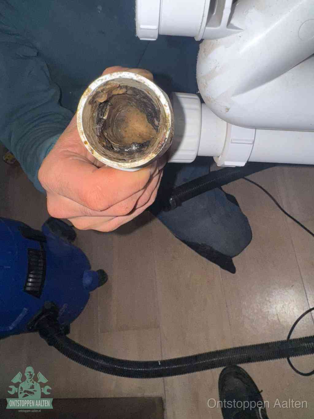 Een hand houdt een losgekoppeld PVC-afvoerbuisstuk vast dat van binnen volledig is dichtgeslibd met vet, vuil en aanslag, de meest voorkomende oorzaak van een verstopte afvoer in Aalten