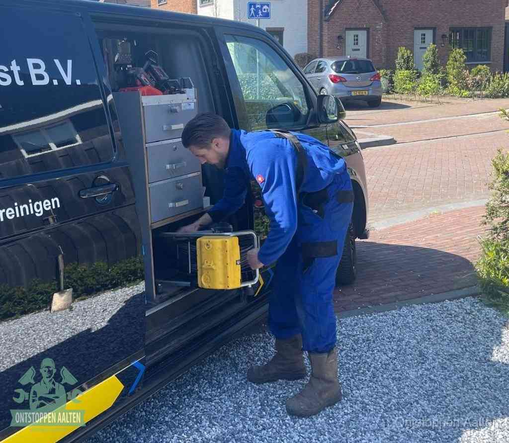 Een monteur pakt buiten op de oprit gereedschap uit de bedrijfsbus, het moment om een professional in te schakelen voor een verstopte afvoer in Aalten