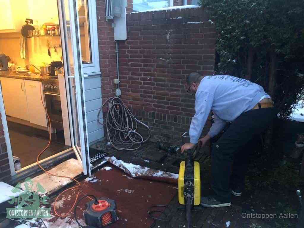 Een monteur werkt buiten bij een open riool-/grondput met een elektrische ontstoppingsmachine om een verborgen afvoerprobleem op te sporen in Aalten