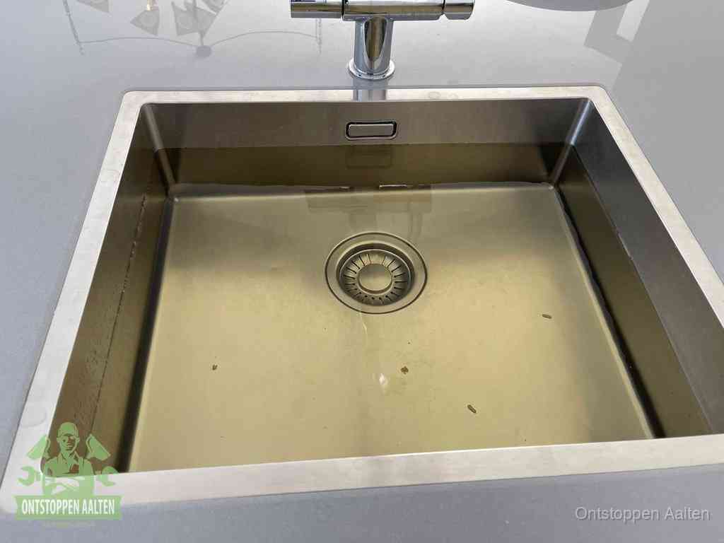 Stilstaand water in een rvs spoelbak dat niet wegloopt, een duidelijk signaal van een gootsteenverstopping in Aalten