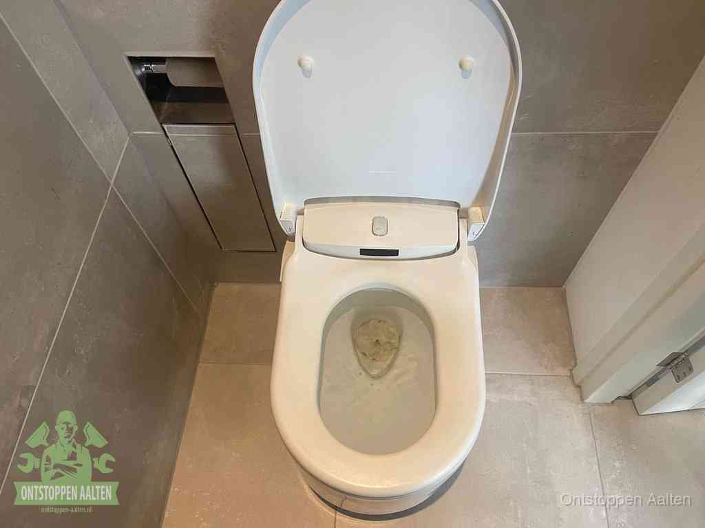 Een wit hangtoilet waarin een prop wc-papier op het water blijft drijven, een duidelijk signaal van een verstopte wc in Aalten