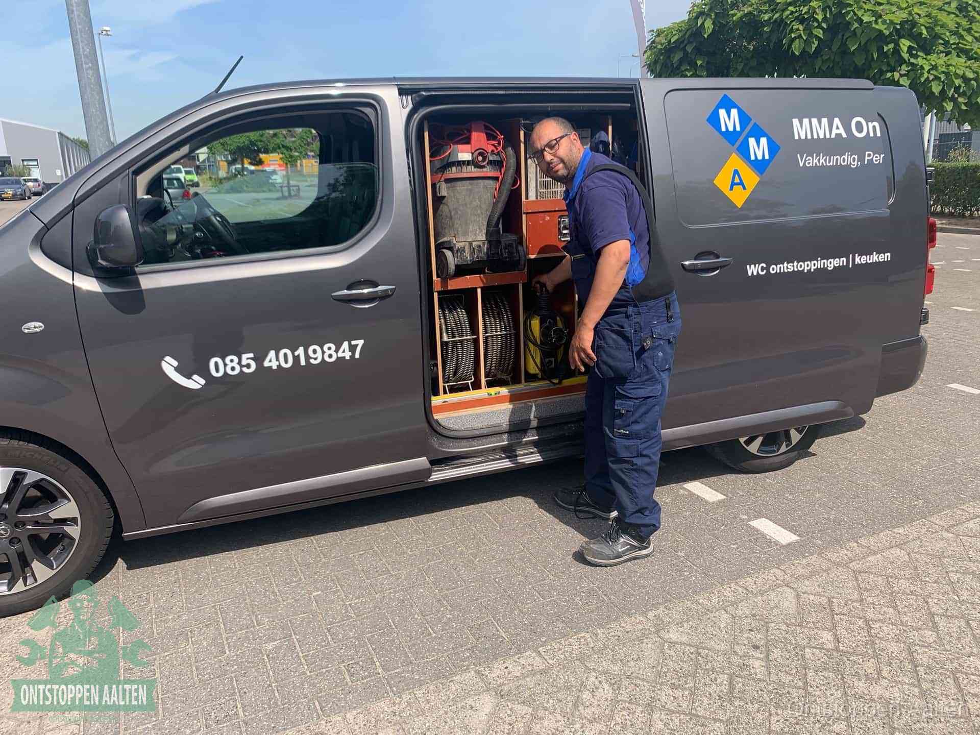 Een monteur bij de open schuifdeur van zijn bedrijfsbus op een parkeerplaats, klaar om de oorzaak van terugkerende afvoerverstoppingen aan te pakken in Aalten