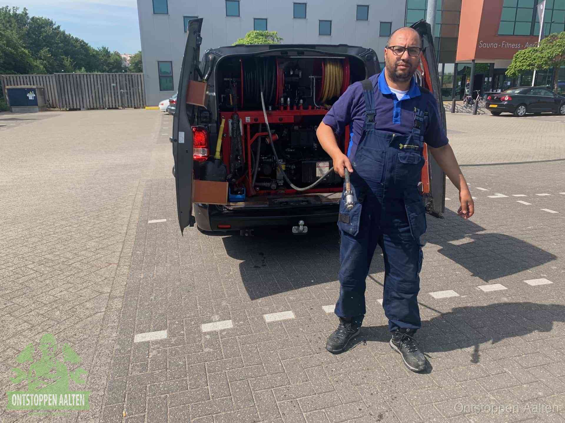 Een monteur bij zijn bestelbus met een hogedruk- en rioolreinigingsunit, klaar om de oorzaak van terugkerende wc-verstoppingen aan te pakken in Aalten
