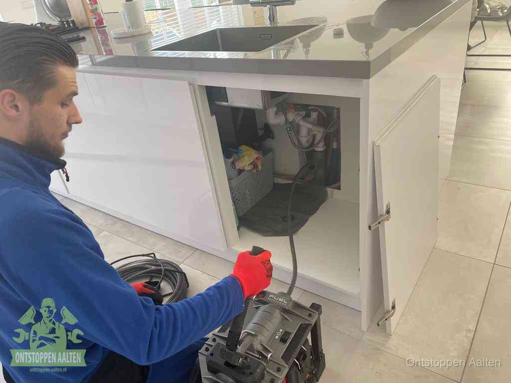 Monteur ontstopt met een veermachine een verstopte afvoer onder de gootsteen in Aalten