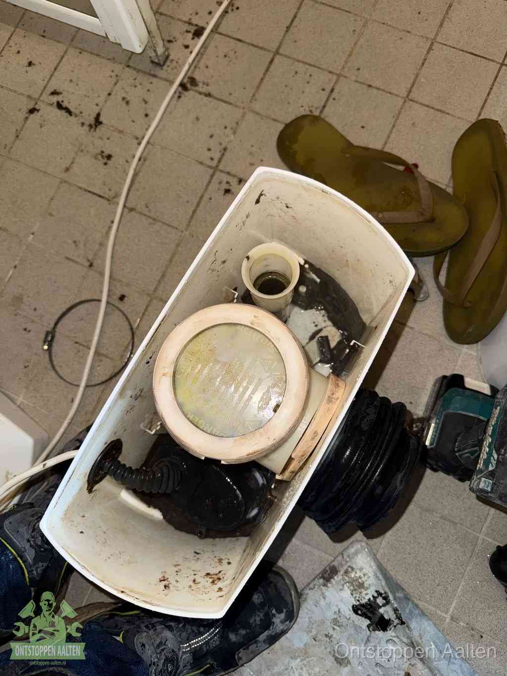 Een gedemonteerde toiletpot op de vloer met ontstoppingsveer en gereedschap ernaast, het verwijderen van een vastzittend voorwerp uit de wc in Aalten