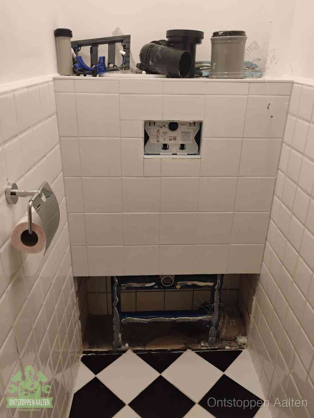 Een toiletruimte waar het hangtoilet en de inbouwreservoir-onderdelen zijn vrijgelegd voor onderhoud, periodiek nazicht voorkomt een wc-verstopping in Aalten