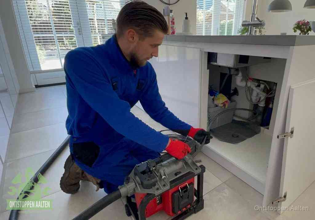 Een monteur voert een professionele elektrische ontstoppingsmachine in de afvoer onder de spoelbak tijdens het gootsteen ontstoppen in Aalten
