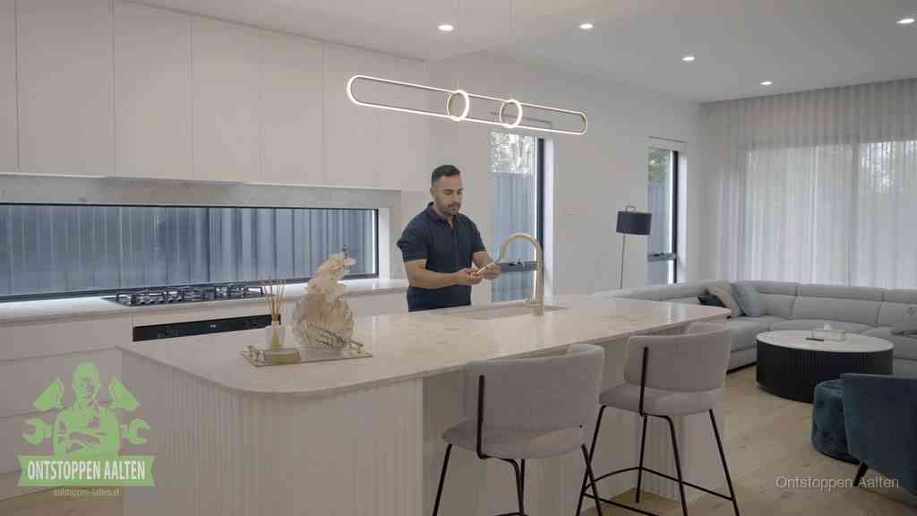 Een bewoner bij de keukenspoelbak die zelf aan de slag gaat met een verstopte gootsteen in Aalten