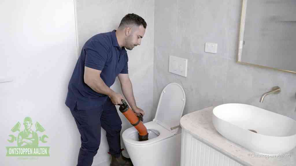 Een man gebruikt een handmatige luchtdruk-ontstopper in een modern betegeld toilet om zelf de wc te ontstoppen in Aalten